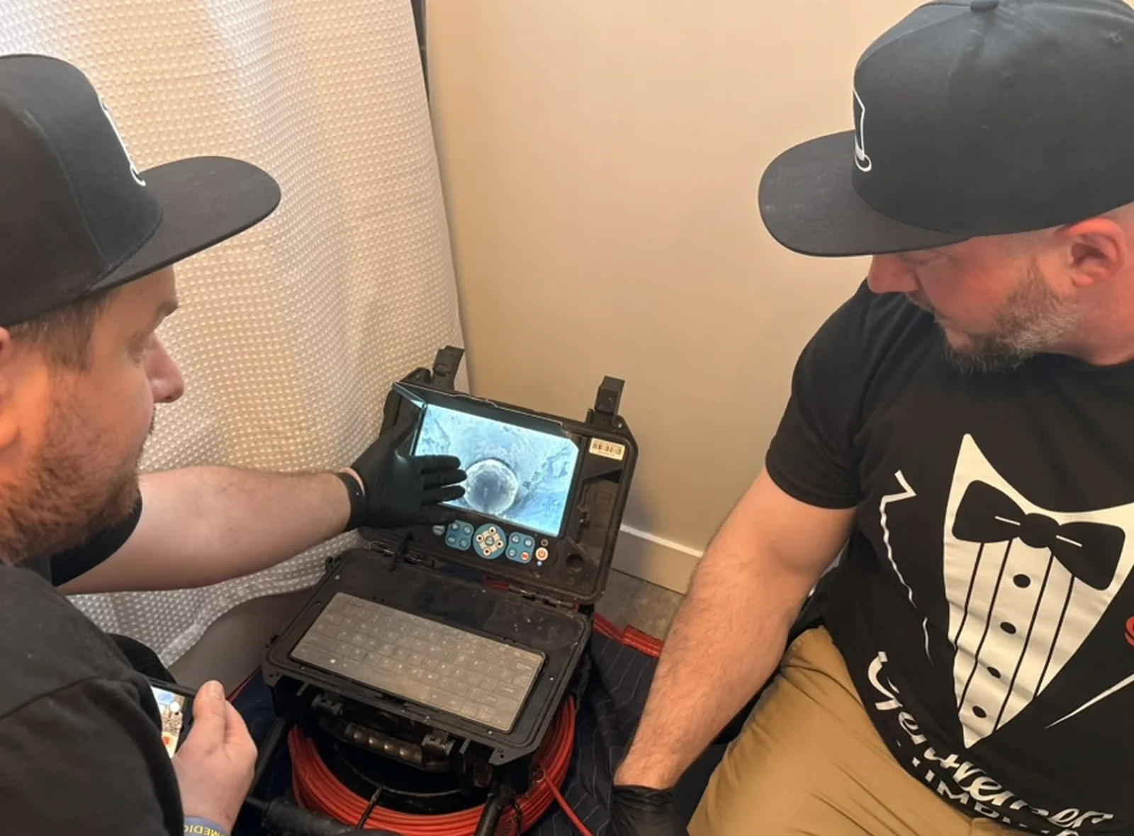 Two plumbing technicians reviewing sewer camera inspection footage on a monitor