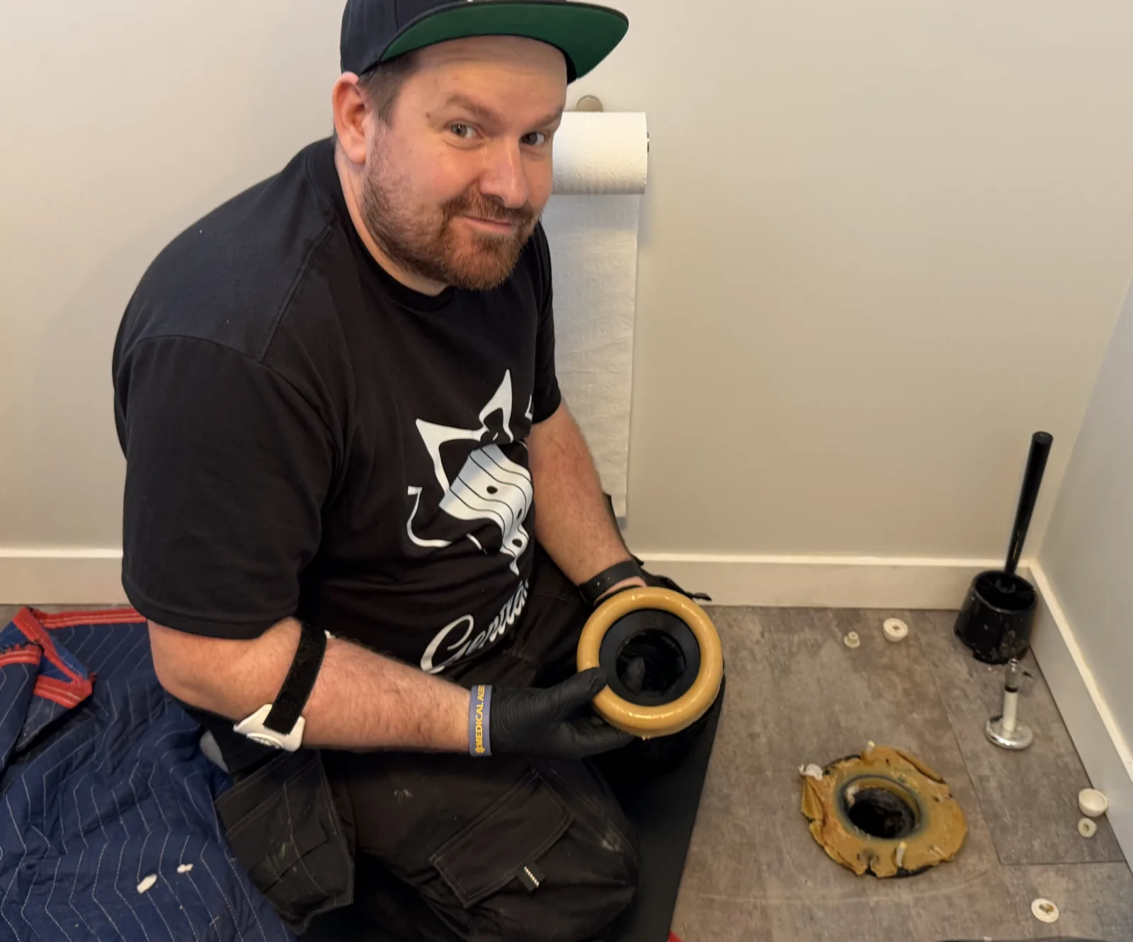 Plumber holding a new wax ring for a toilet reseal with the old wax ring on the floor