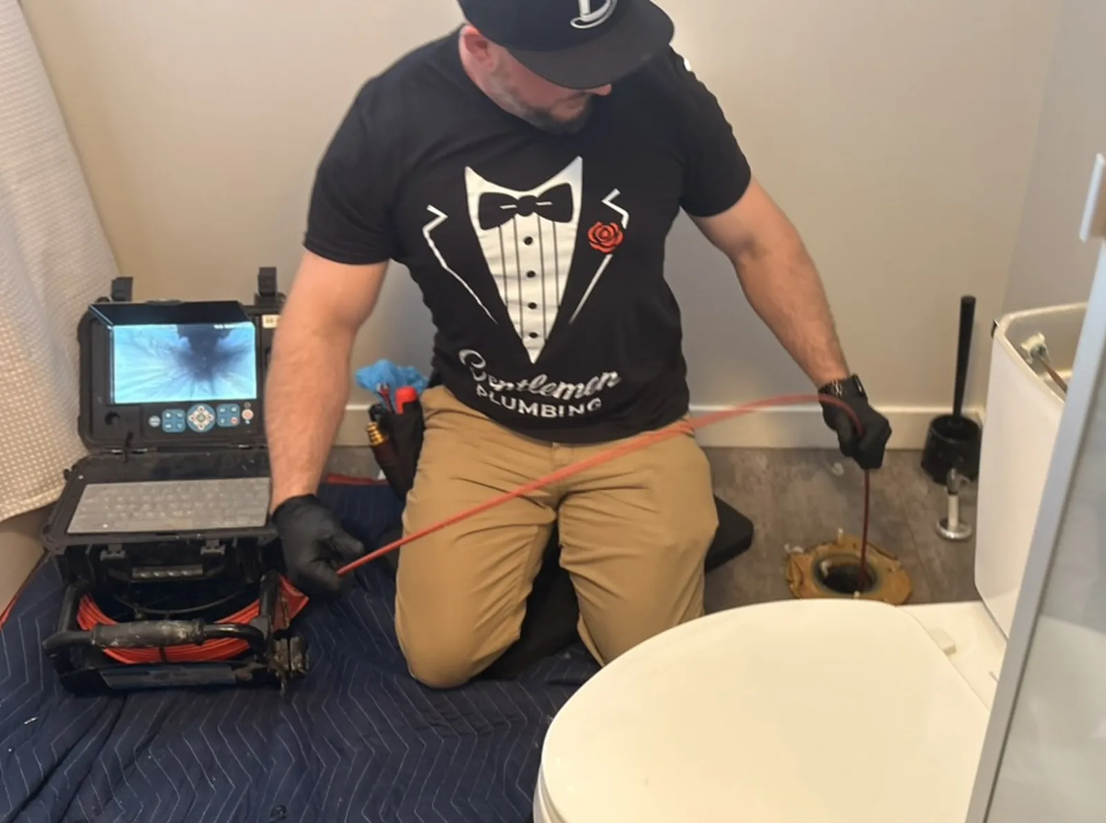 Plumber feeding a drain camera cable into an exposed toilet flange.