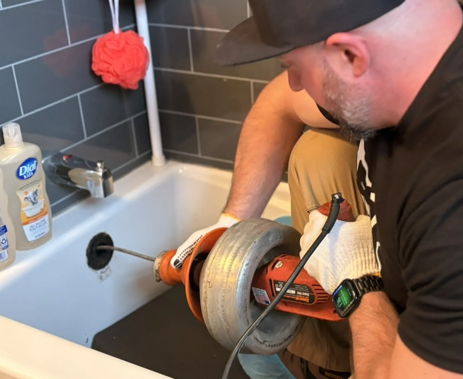 Plumber feeding a drain snake into a bathtub overflow opening.