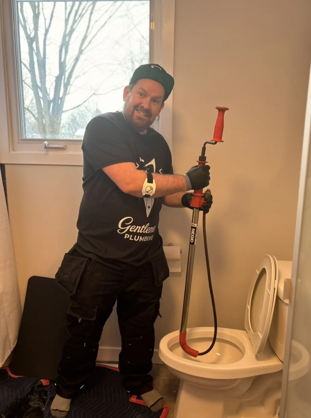 Gentlemen Plumbing technician holding a toilet auger above an open toilet during toilet drain service.