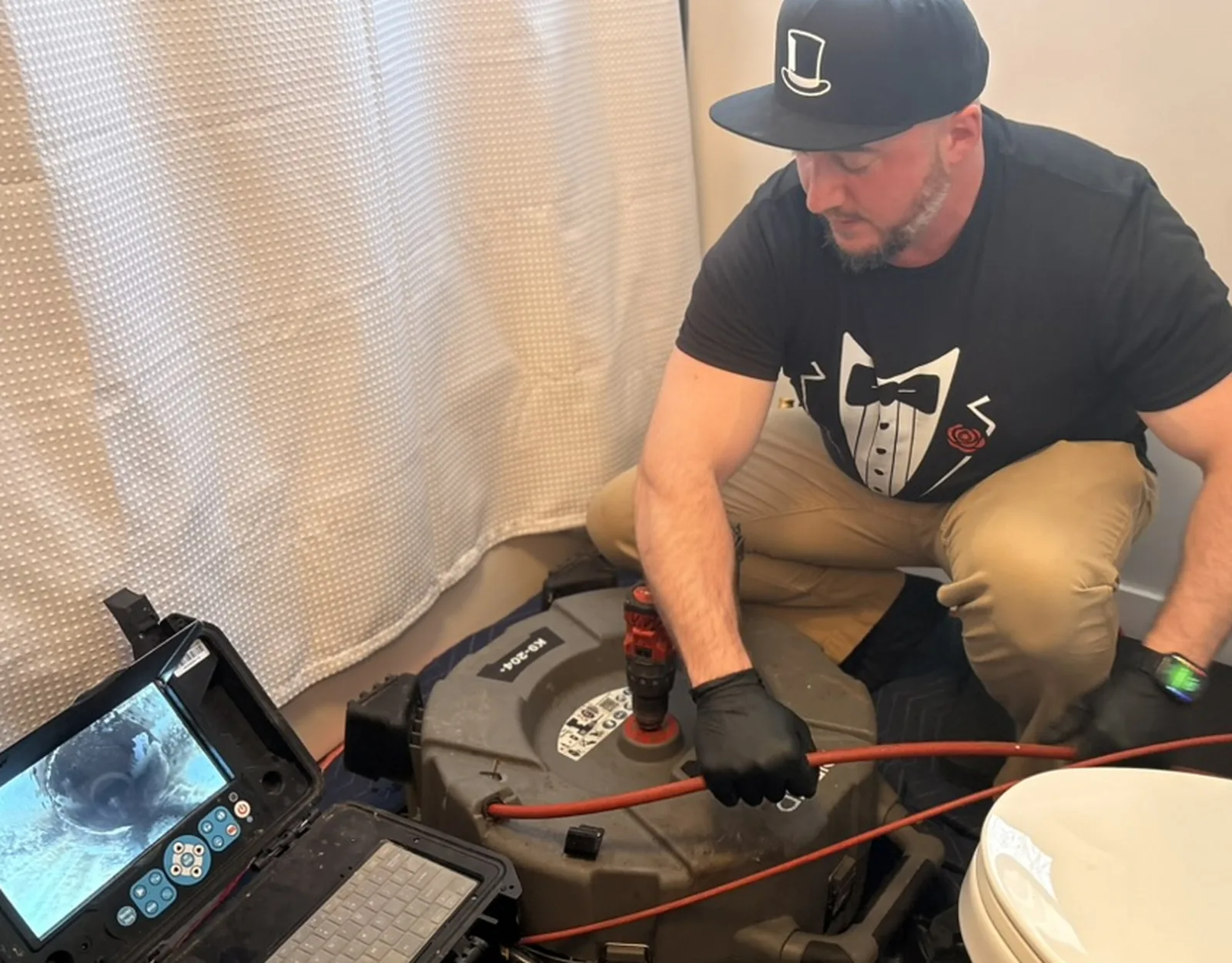 Plumber operating drain camera equipment beside a toilet.