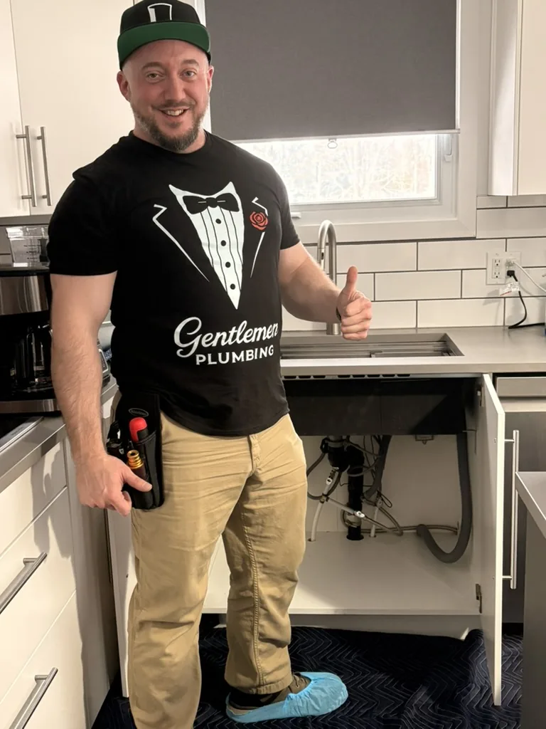Plumber standing by an open kitchen sink cabinet.