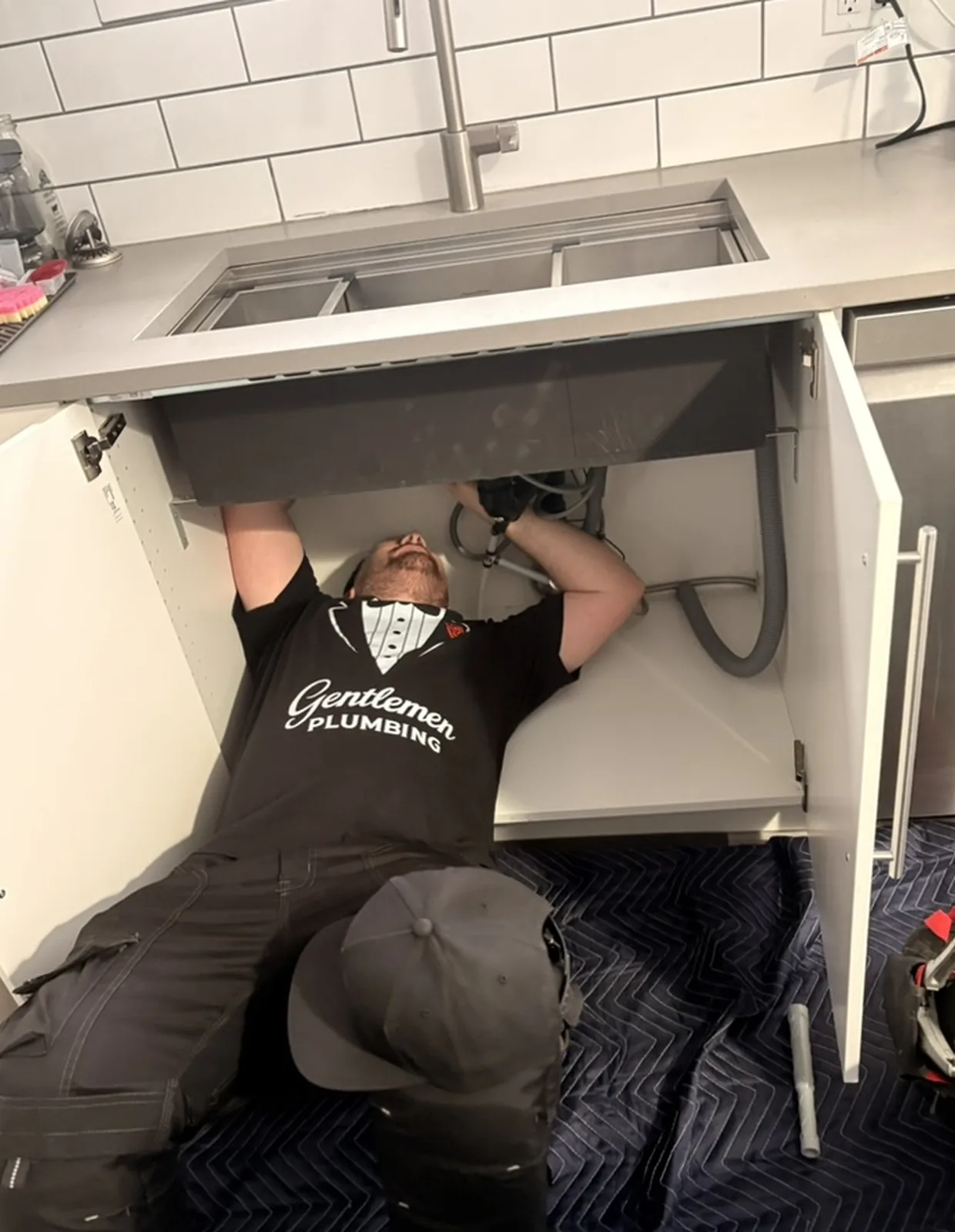 Plumber working under a kitchen sink from the floor.
